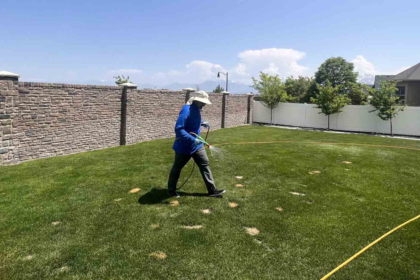 tech with a fence behind him spraying on a grass patchy grass