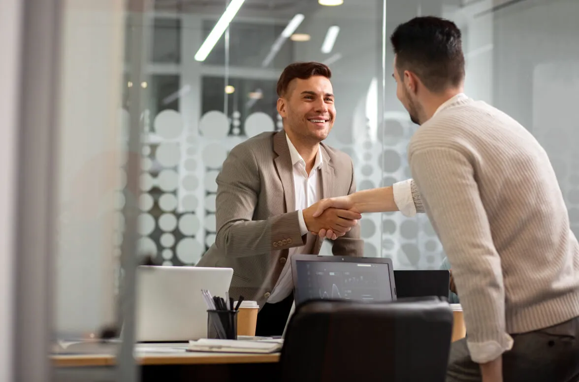 Dos hombres jóvenes en una oficina moderna se dan la mano y sonríen durante una reunión de negocios.