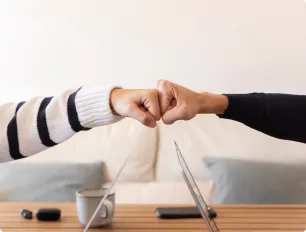 Dos personas chocando los puños sobre una mesa con tazas y una computadora portátil.