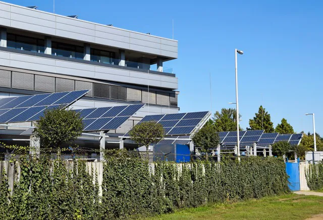 Paneles solares instalados frente a un edificio moderno con follaje y cielo azul despejado.