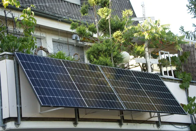 Paneles solares instalados en el balcón de una casa con vegetación alrededor.