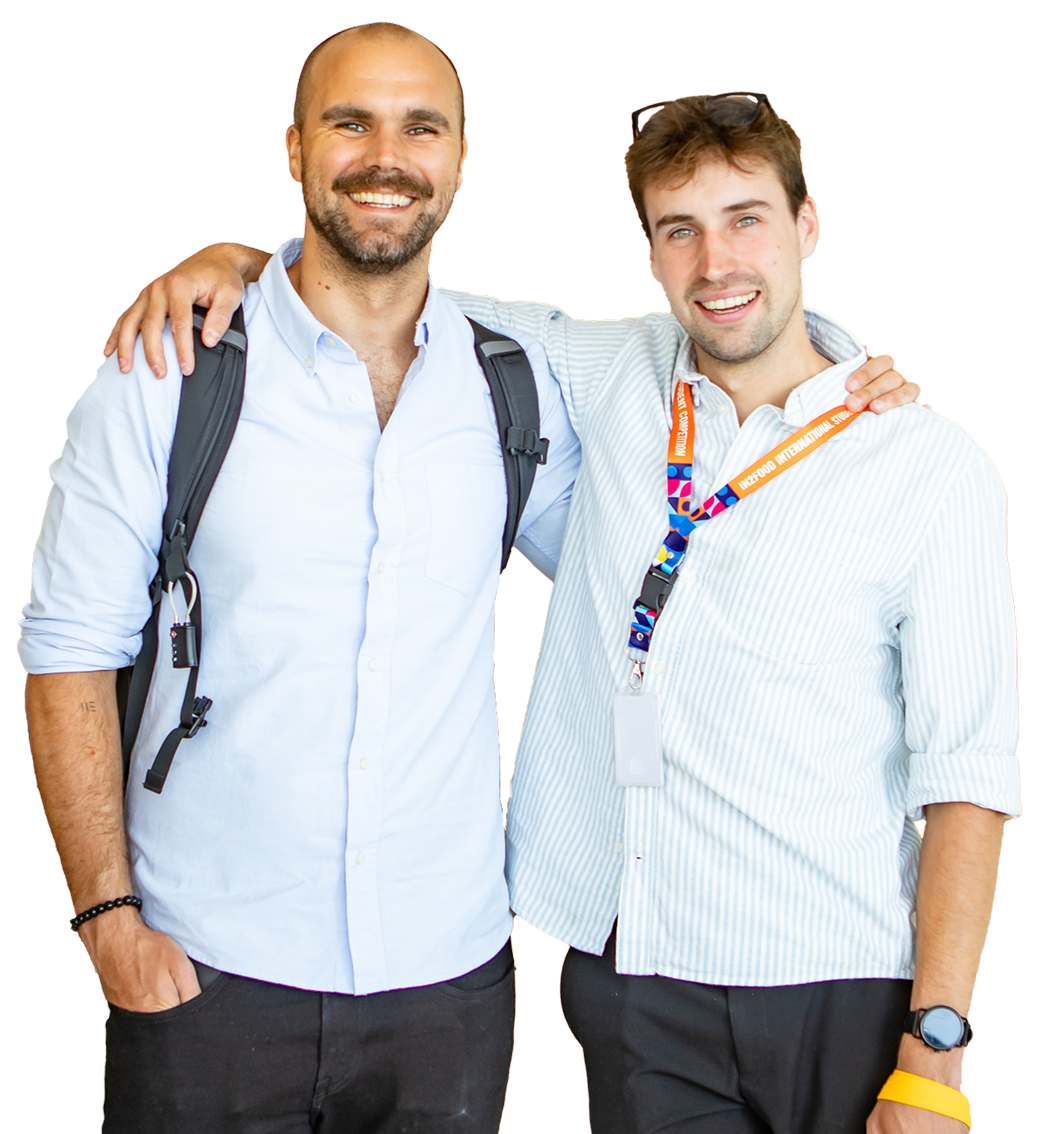 Two guys wearing a badge and a shirt, both are smiling.