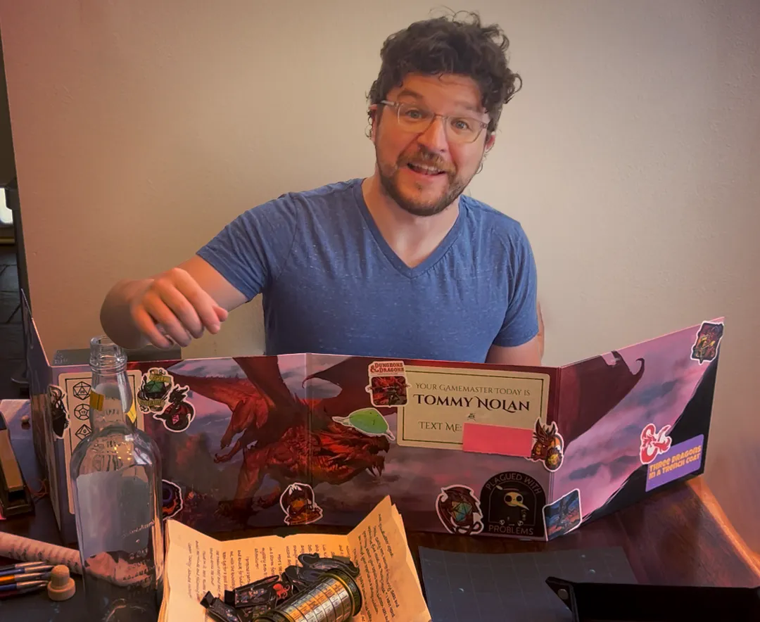 Tommy Nolan as a dungeon master behind a DM screen with props, puzzles, and dice scattered around a table.