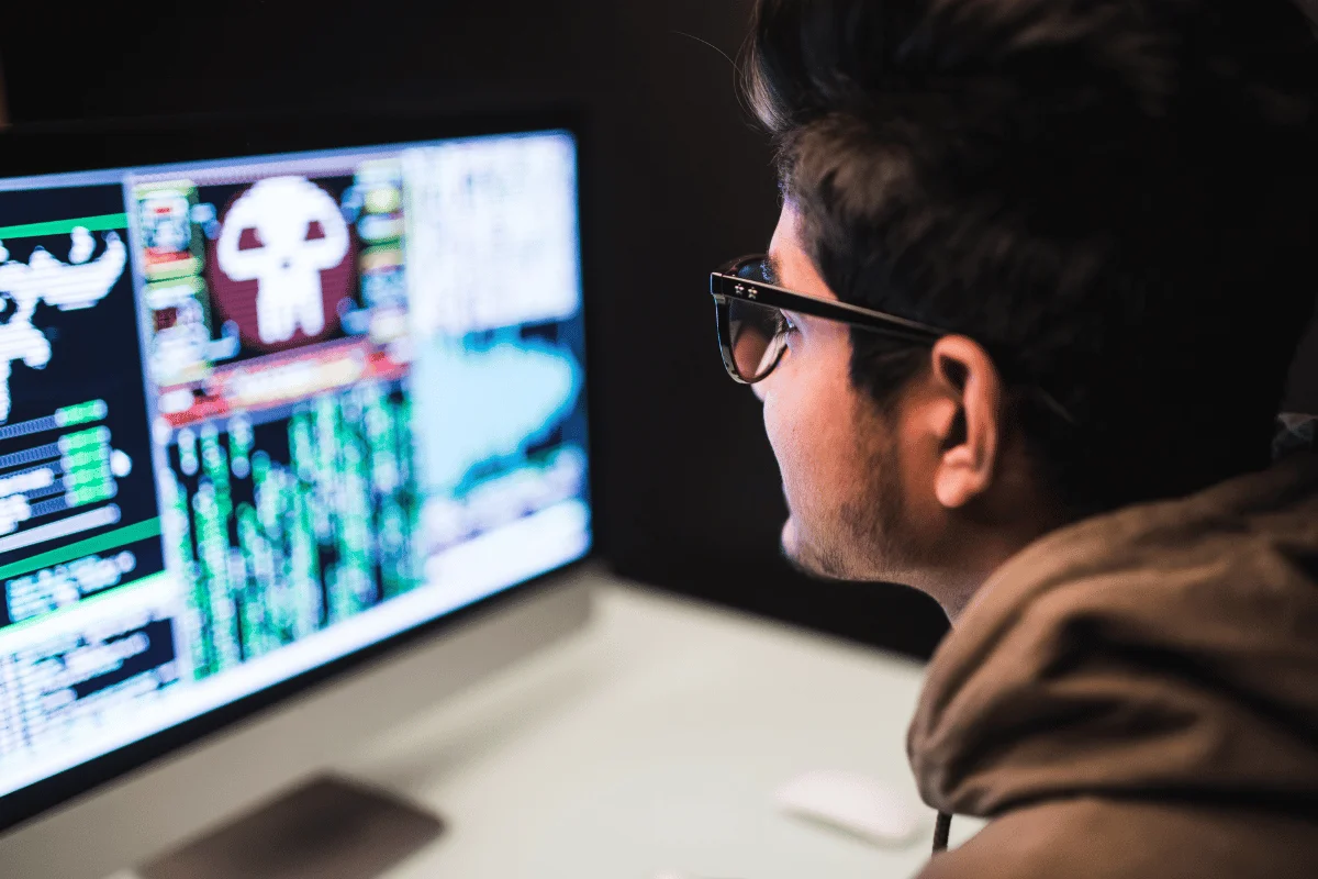 A person wearing glasses intensely focuses on a computer screen displaying complex data and graphics. The scene conveys concentration and technological engagement.