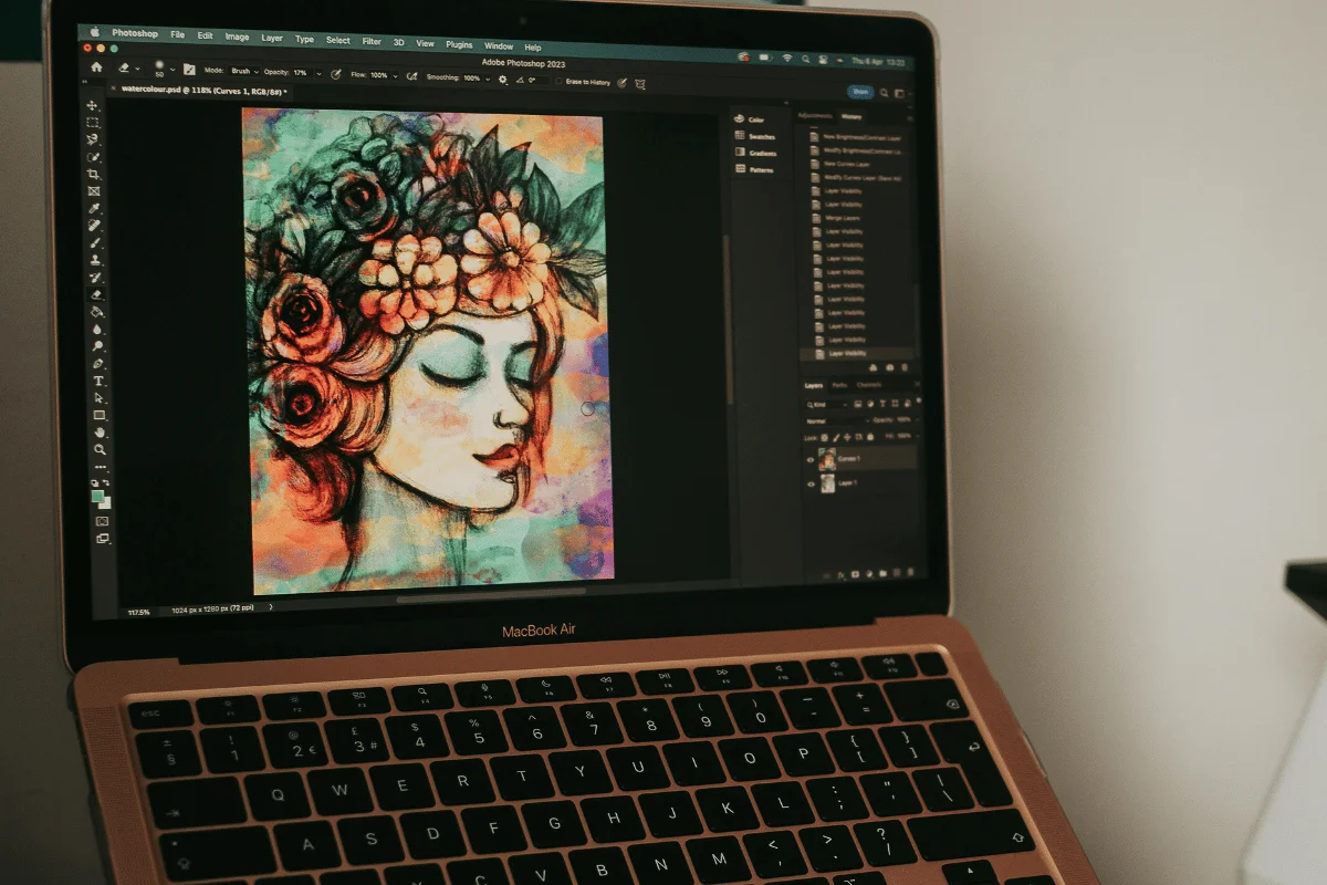 A laptop displays digital artwork in Adobe Photoshop, featuring a serene female portrait with flowers in her hair. The image is vibrant and colorful.