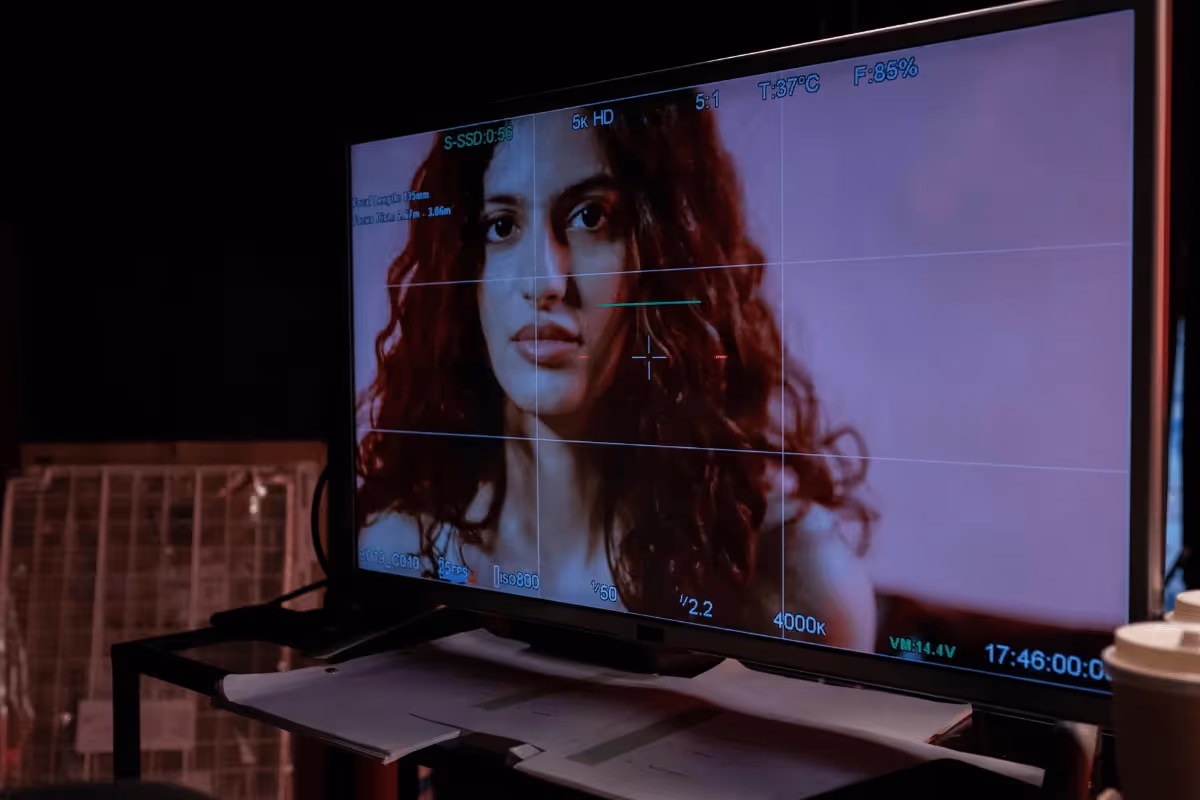 A monitor displays a scene with a person having long, curly red hair, set against a dimly lit background with technical settings visible.