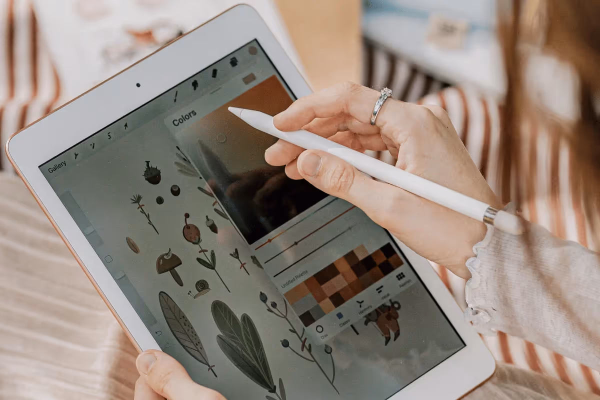 A person using a stylus on a tablet displaying nature-themed digital illustrations and a color palette, conveying creativity and focus.