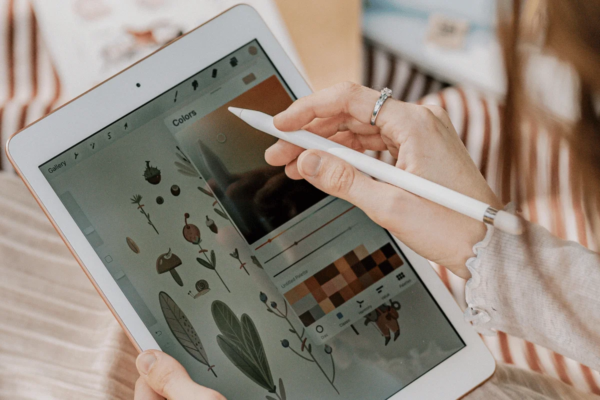 A person using a stylus on a tablet displaying nature-themed digital illustrations and a color palette, conveying creativity and focus.