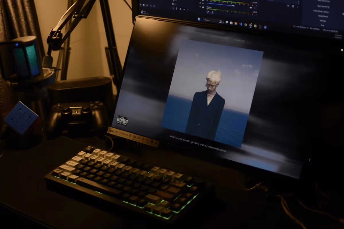 A gaming setup featuring a keyboard, game controller, and a monitor displaying an album cover with an ocean background.