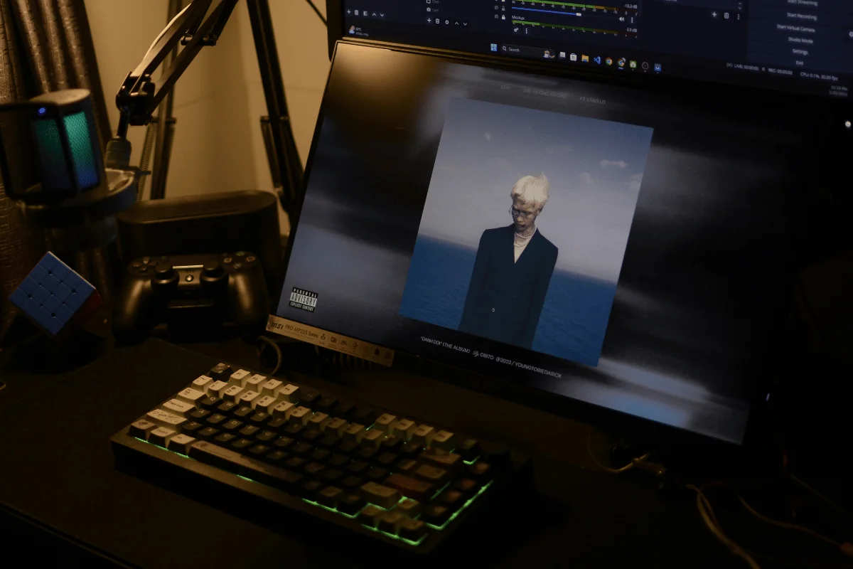 A gaming setup featuring a keyboard, game controller, and a monitor displaying an album cover with an ocean background.