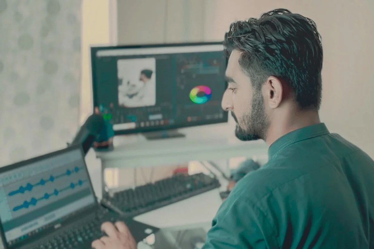 A man in a green shirt works on a laptop with audio software displayed. 