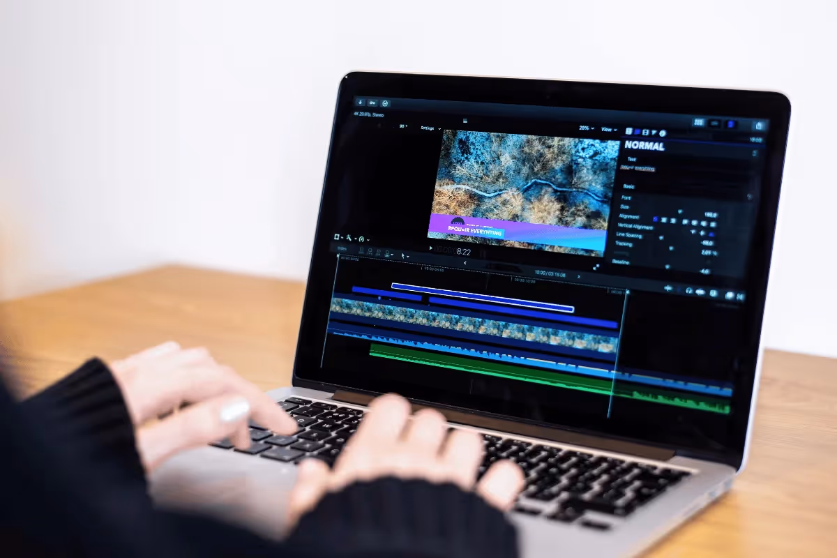 A person edits a nature video on a laptop. The screen displays editing software with timelines and color adjustments. The setting is bright and focused.