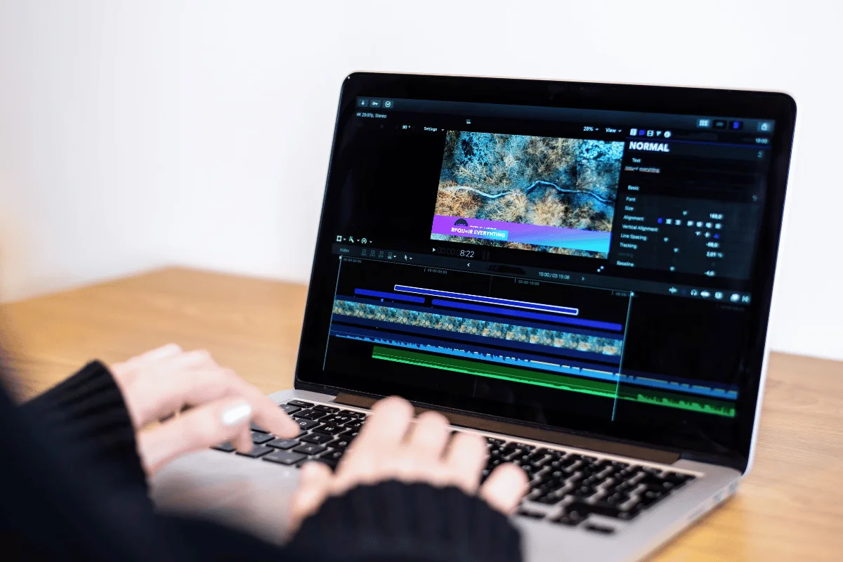 A person edits a nature video on a laptop. The screen displays editing software with timelines and color adjustments. The setting is bright and focused.
