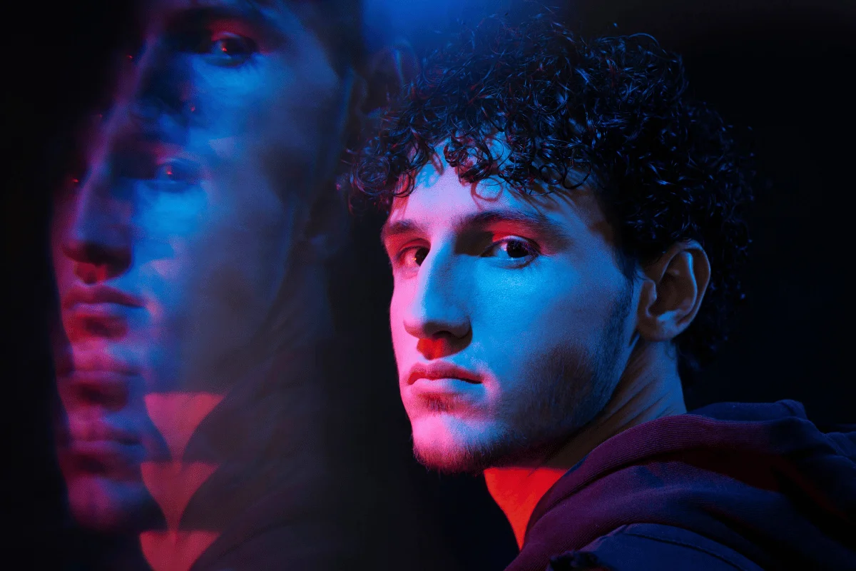 Man’s face illuminated by neon lights with a blurred mirrored reflection.