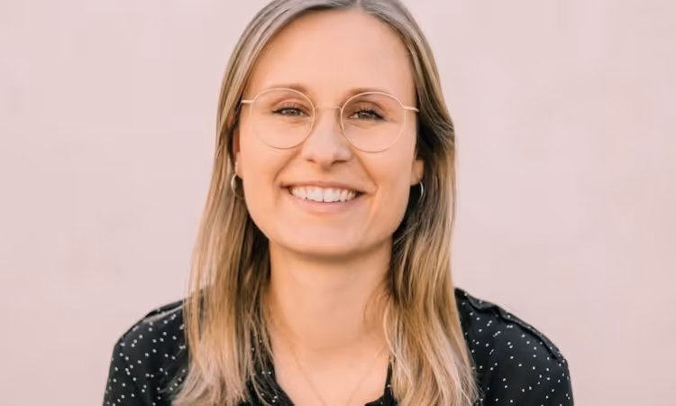 Portrait of Andrea Schneller, co-founder and CEO of koorvi, smiling in front of a light background. She is wearing a dark blouse with small dots.