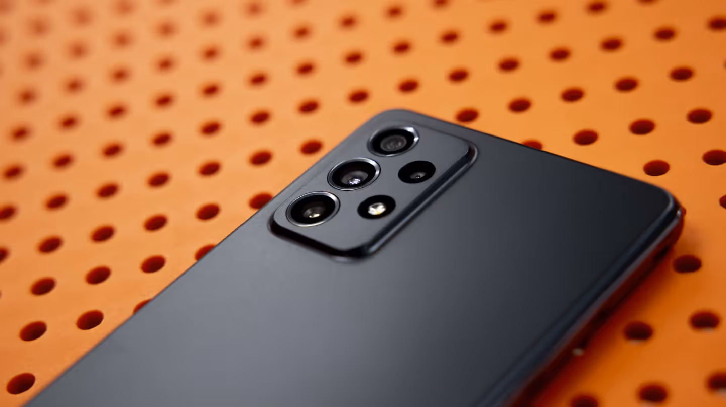 Close-up of the back of a modern black smartphone with multiple camera lenses, placed on an orange perforated surface.