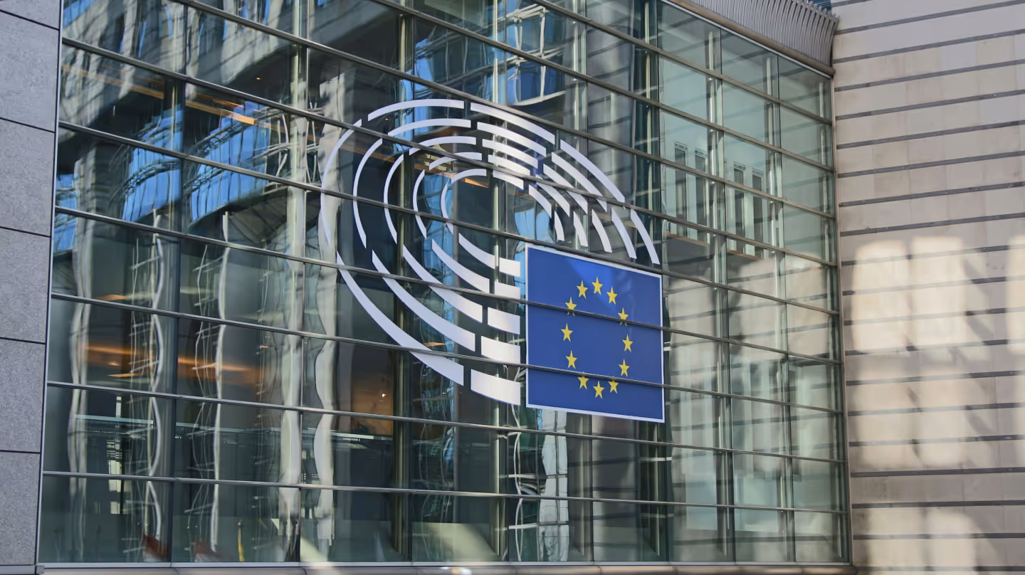 Glass facade of the European Parliament with EU flag and logo.