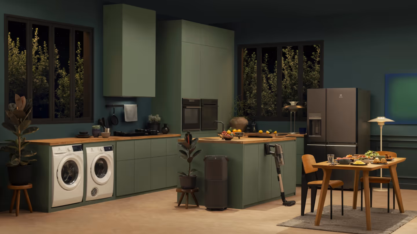 Stylish green kitchen with Electrolux appliances including fridge, washer, dryer, and vacuum, representing sustainability and modern living.
