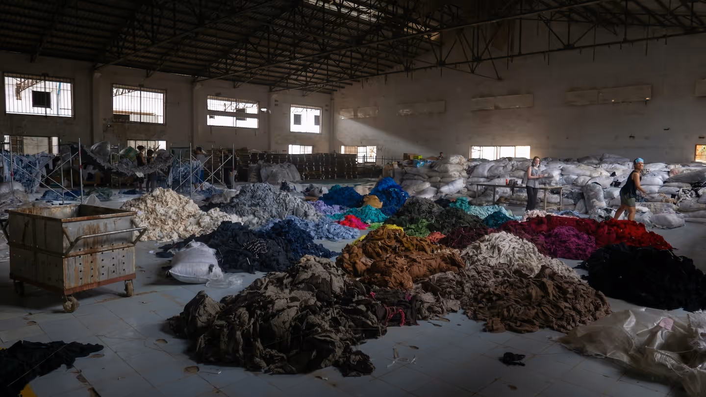 Industrial textile recycling warehouse with colorful piles of sorted fabric waste and worker processing materials