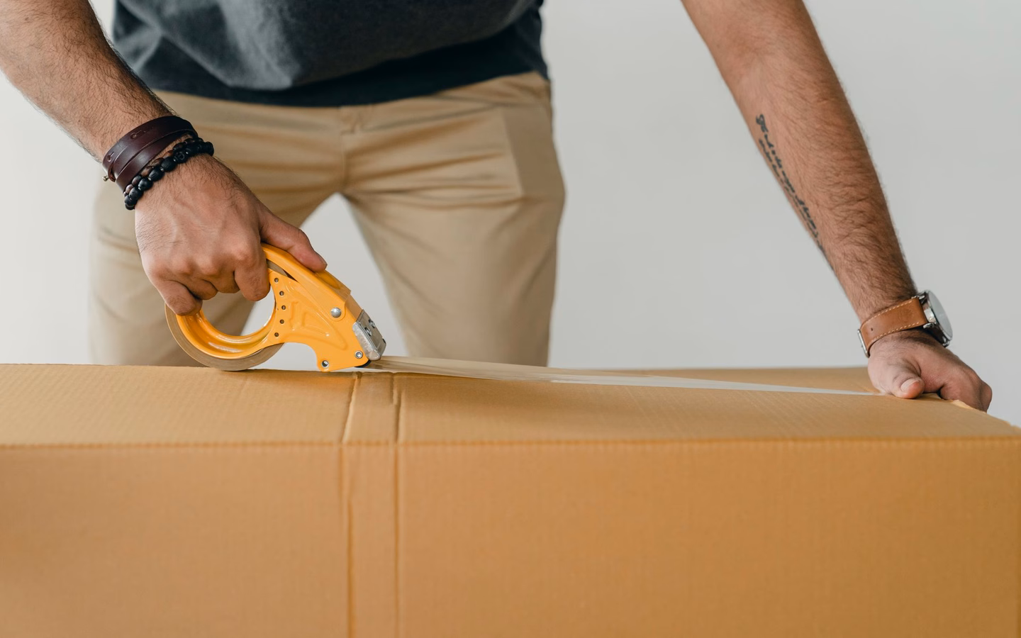 Person verklebt einen großen Versandkarton mit Paketband, um ein Produkt für den Trade-In einzusenden