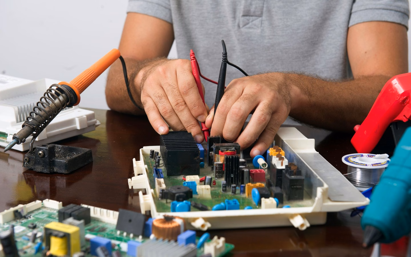Techniker prüft eine Platine mit Multimeter-Messspitzen in einer Refurbishment-Werkstatt