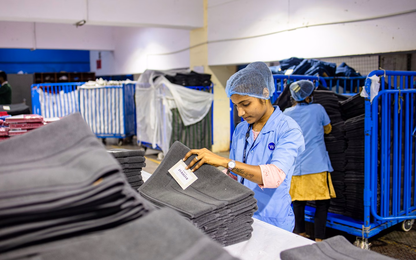 Textile worker grading and labeling folded garments in a warehouse, representing product inspection and refurbishment for resale