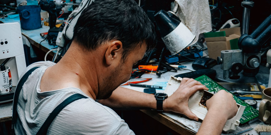 Technician repairing the electronics of a used device at a workbench.