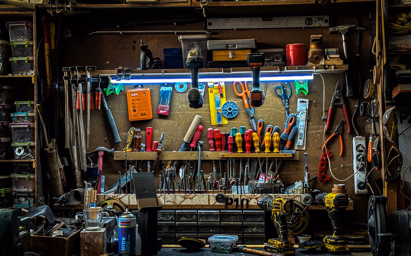 Organised tool and spare parts wall above a workbench in a repair workshop.