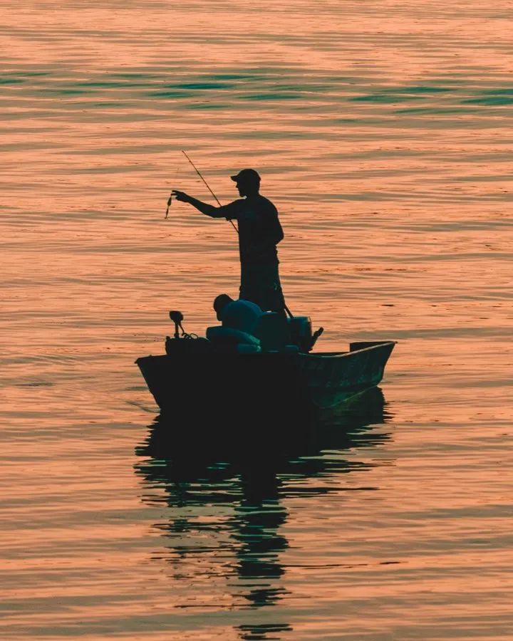 man fishing on boat at sunset