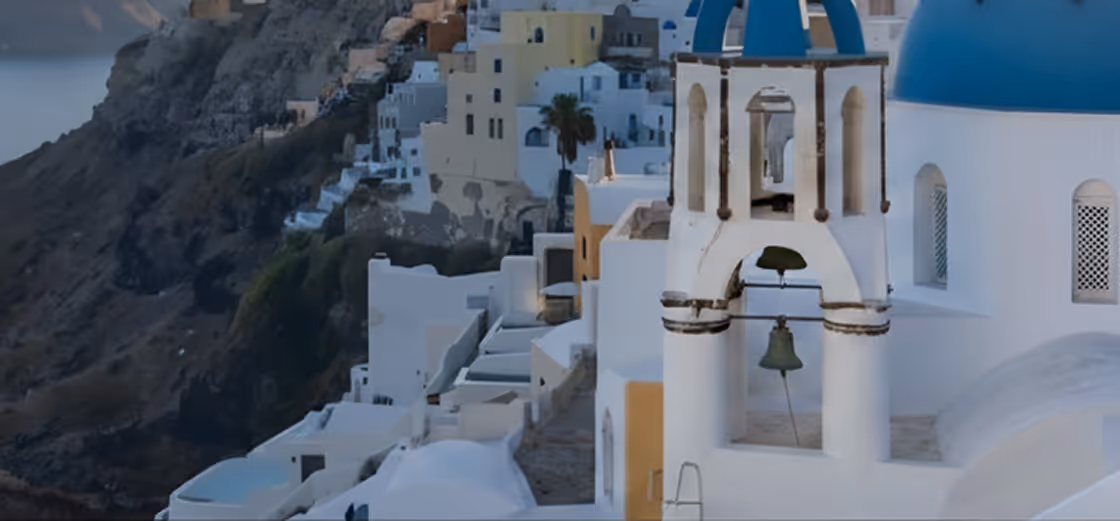 White buildings and blue-domed church with bell tower on a hillside at dusk.