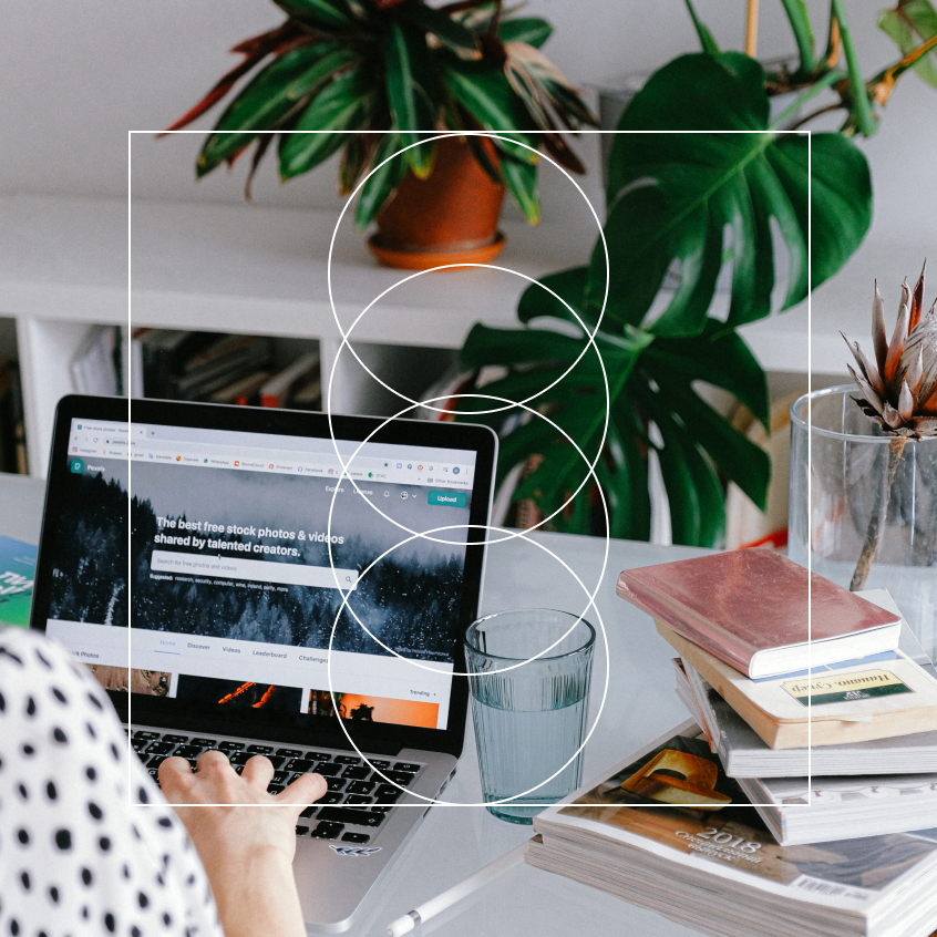 a woman at her desk on her laptop with a plant and a stack of books