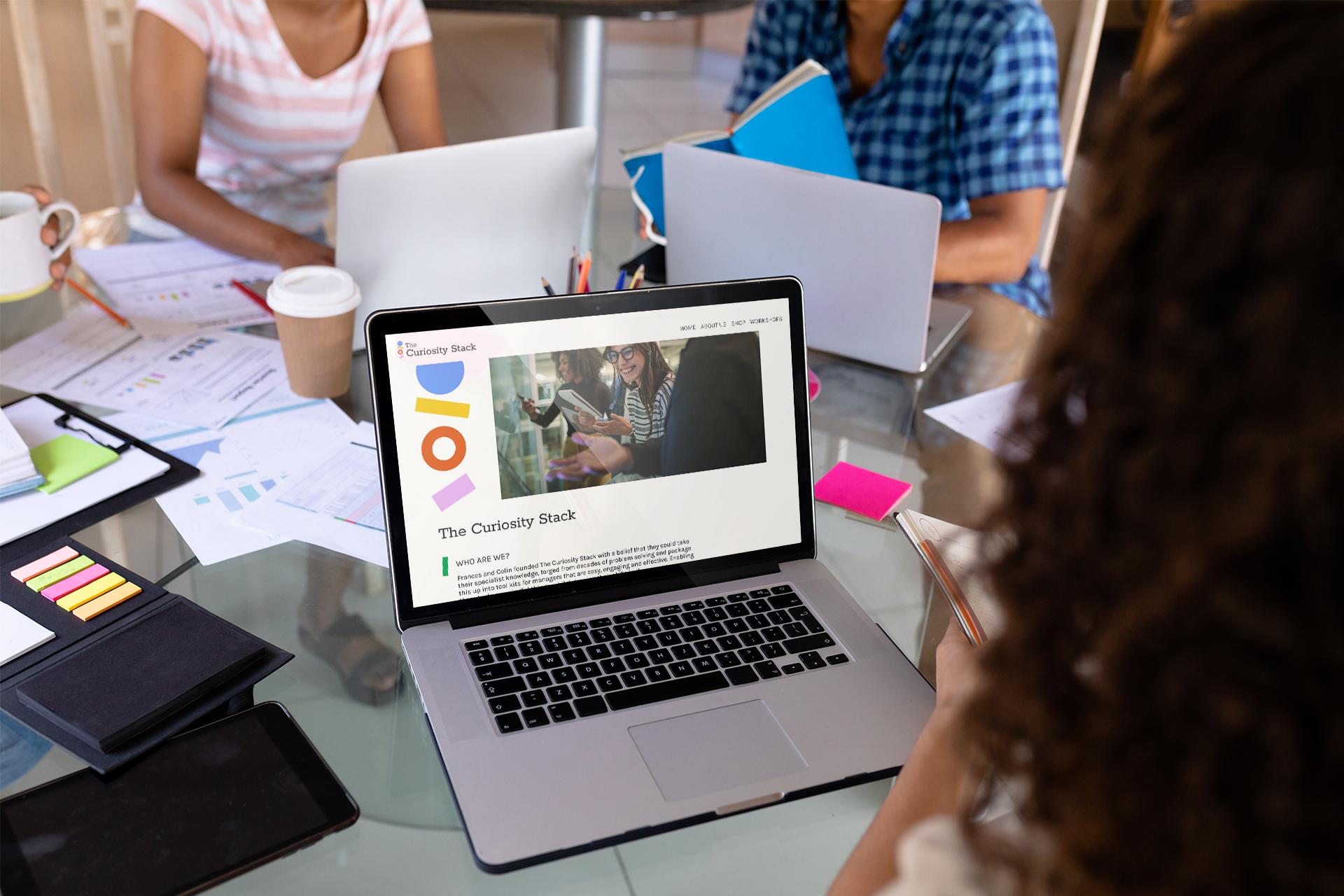 a group of people working together on a table, with one laptop in the centre showing the curiosity stack website