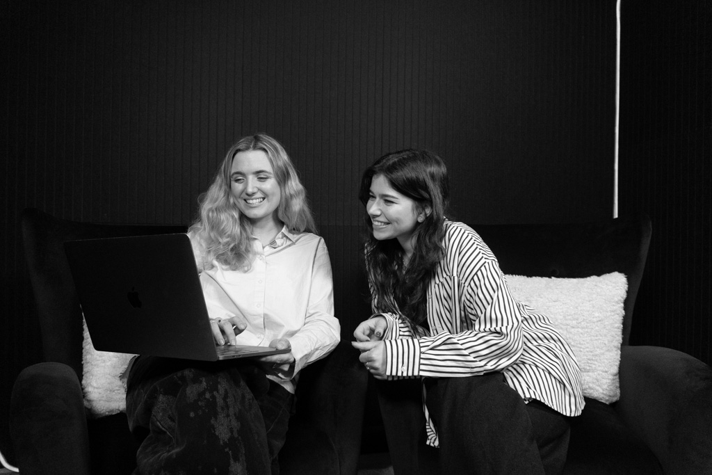 Two team members in the studio smiling looking at a laptop