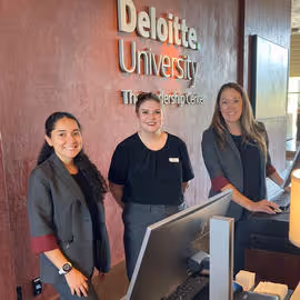 Smiling staff members at the front desk of the Deloitte university