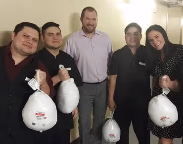 Five people standing indoors holding frozen turkeys and smiling at the camera.