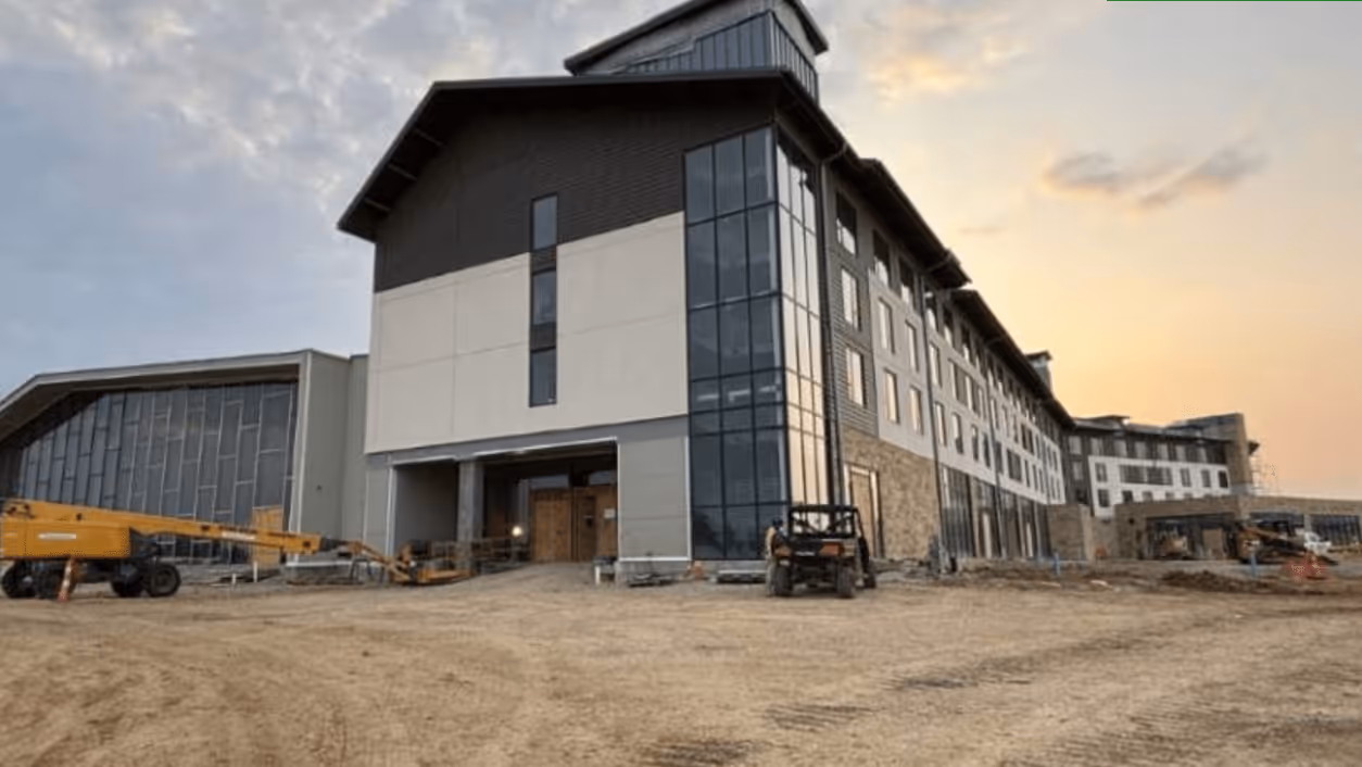 Large modern building under construction with dirt ground and construction equipment at sunset.