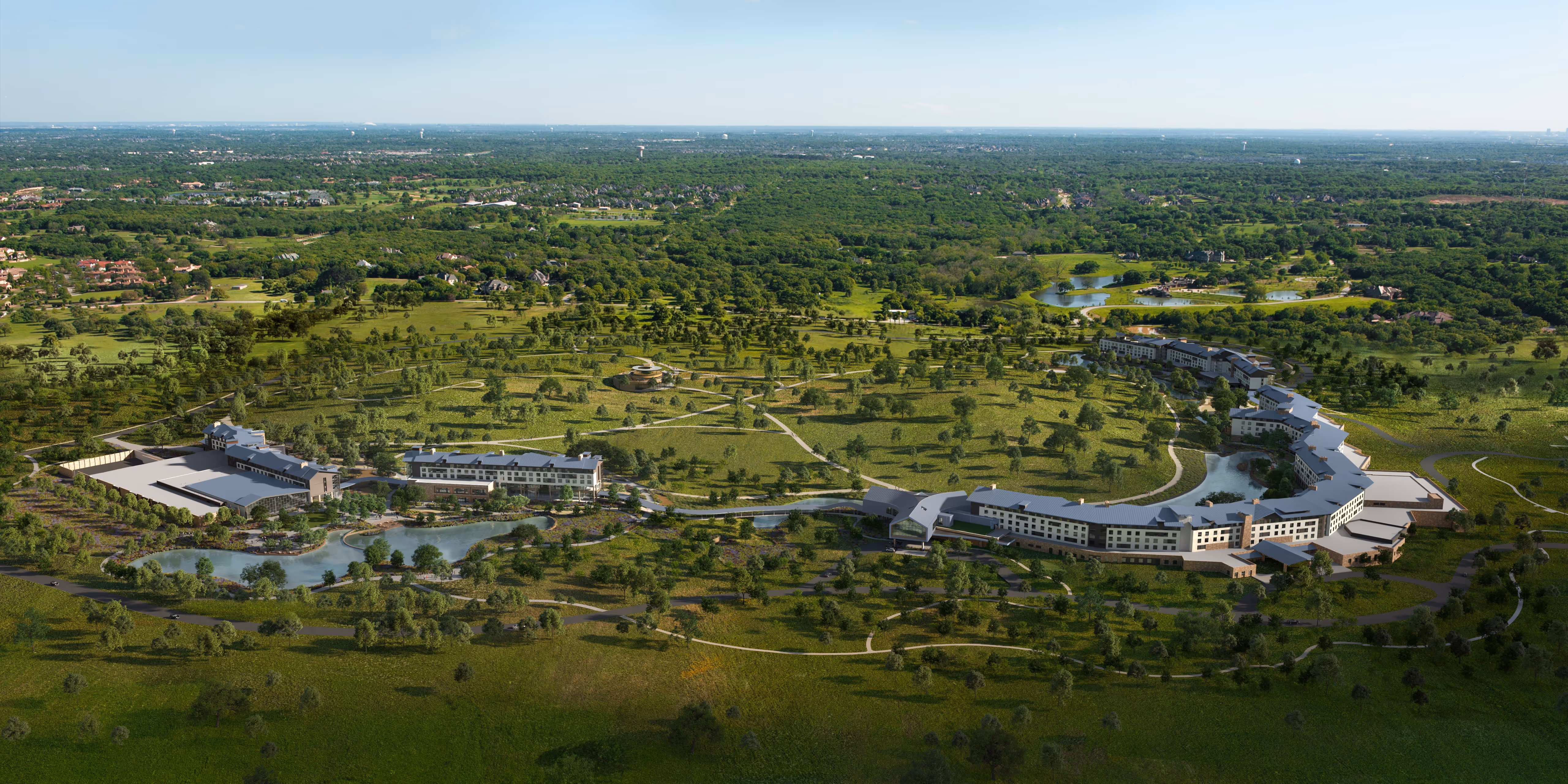 Aerial view of a large modern resort complex surrounded by green fields and trees, featuring multiple buildings connected by walkways and ponds.