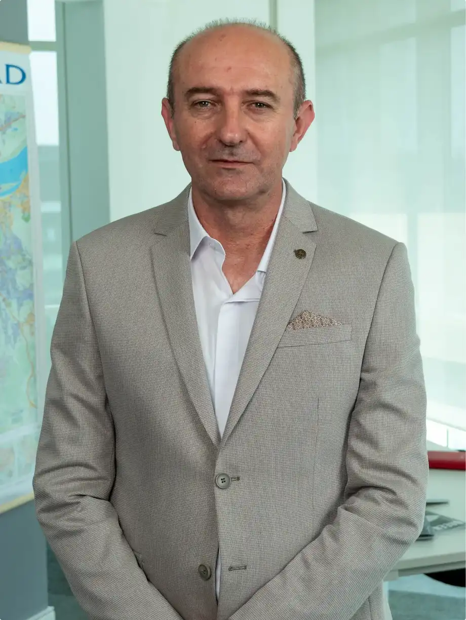 Muškarac srednjih godina u svetlo sivom sakou i beloj košulji stoji unutra.