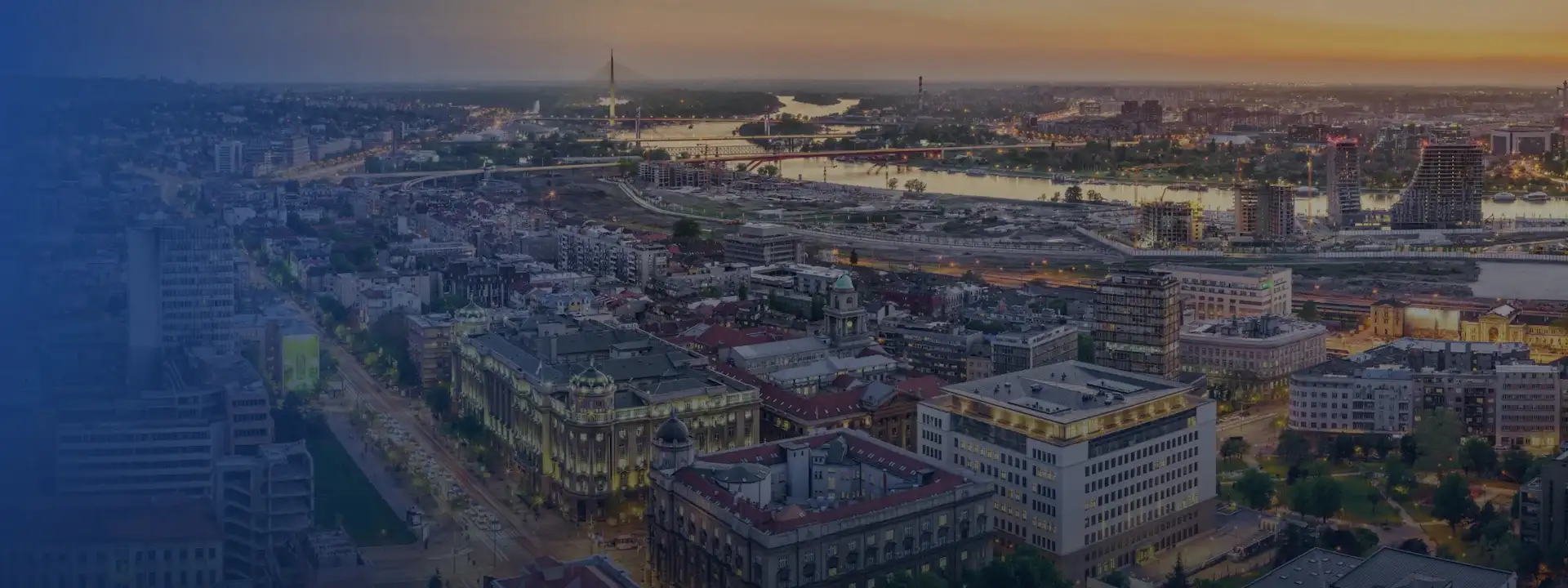 Pogled iz vazduha na gradski pejzaž u suton, sa zgradama, rekom i više mostova.