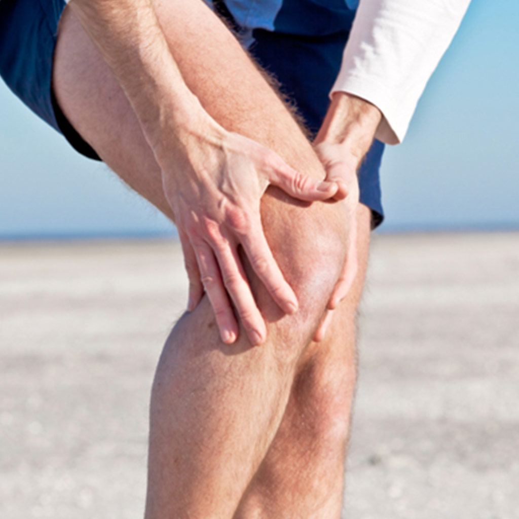 Mann fasst sich am Strand mit beiden Händen an sein Knie
