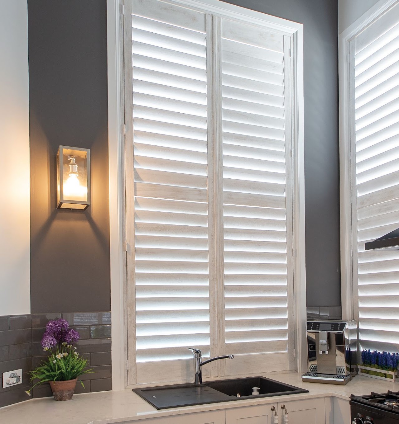 White plantation shutters beside a wall lamp