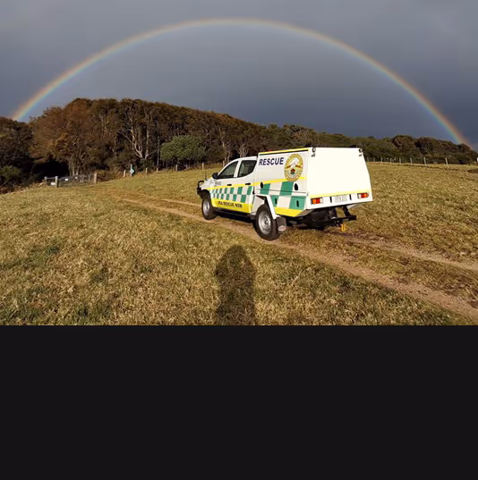 Rescue vehicle parked on a grassy path with a rainbow arching over a forest in the background.