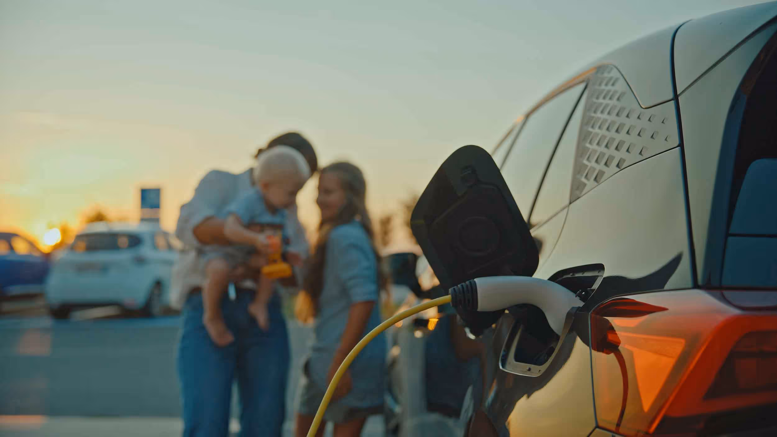 Electric car charging with family in the background during sunset.
