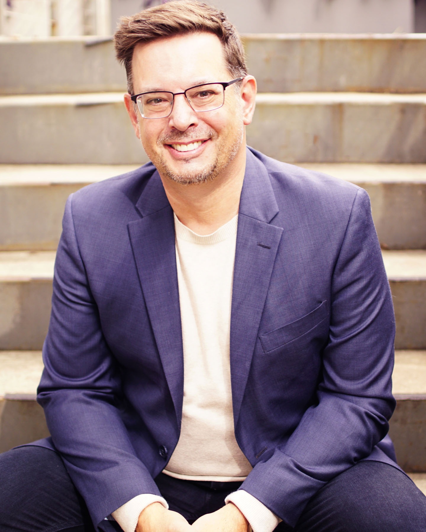 Portrait of Jim Firestone in a navy suit and tshirt sitting on a concrete staircase