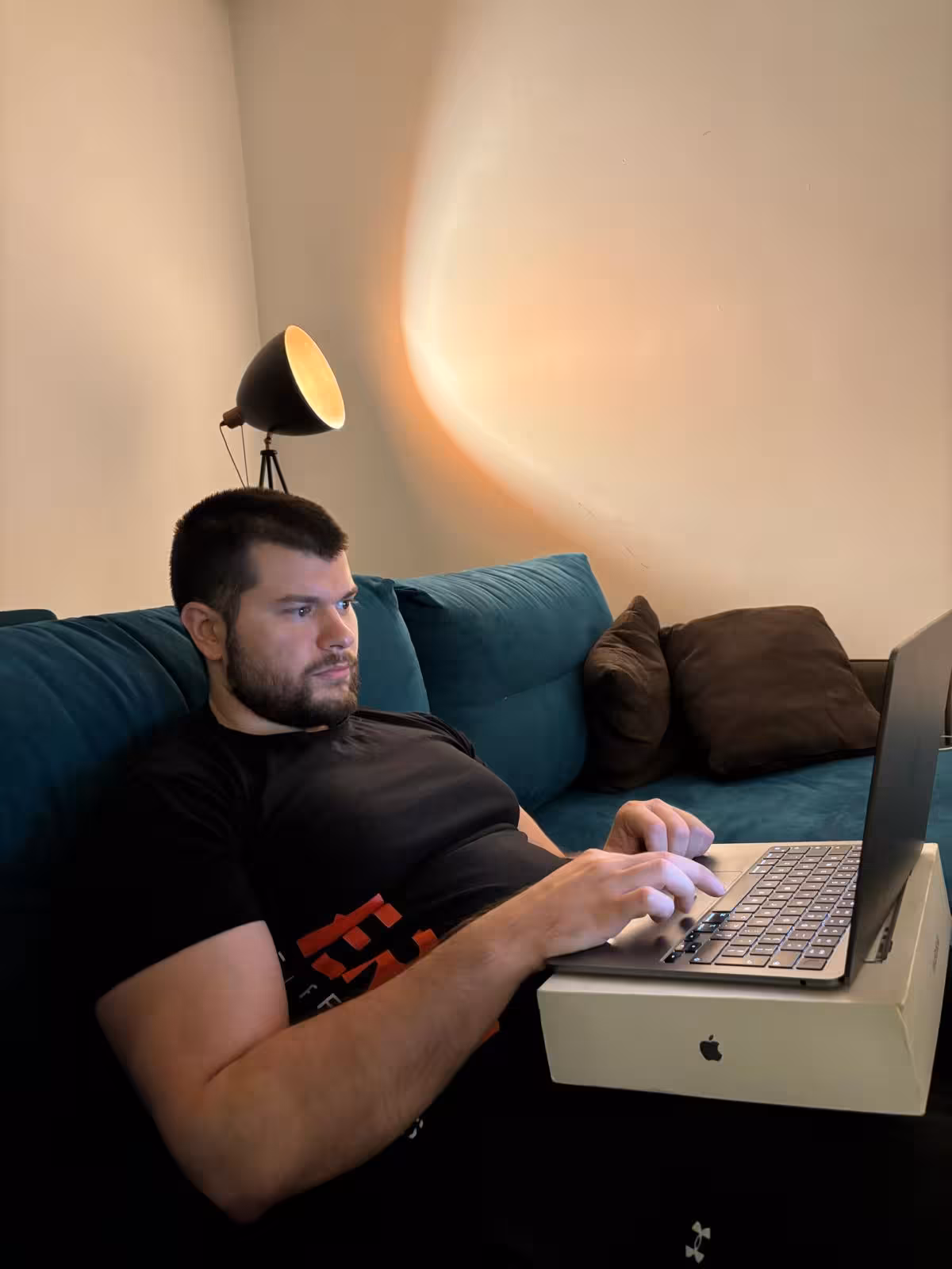 Milan sitting on a couch using a laptop while writing this text, with a floor lamp beside him.
