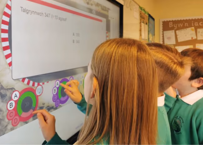 Three young students using an interactive touchscreen in their classroom.
