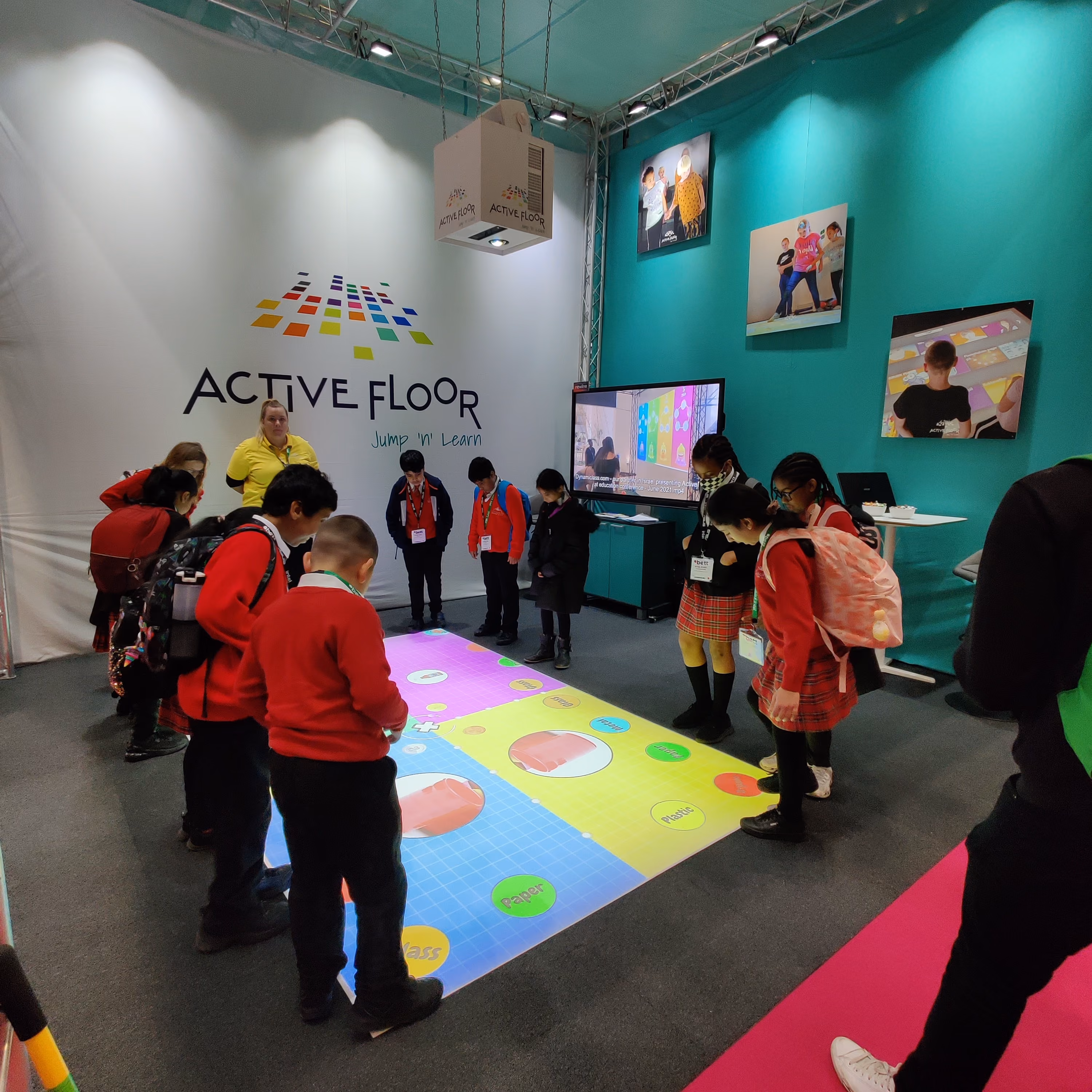 Group of children and an adult interacting with a colorful interactive floor game at an Active Floor exhibit booth.
