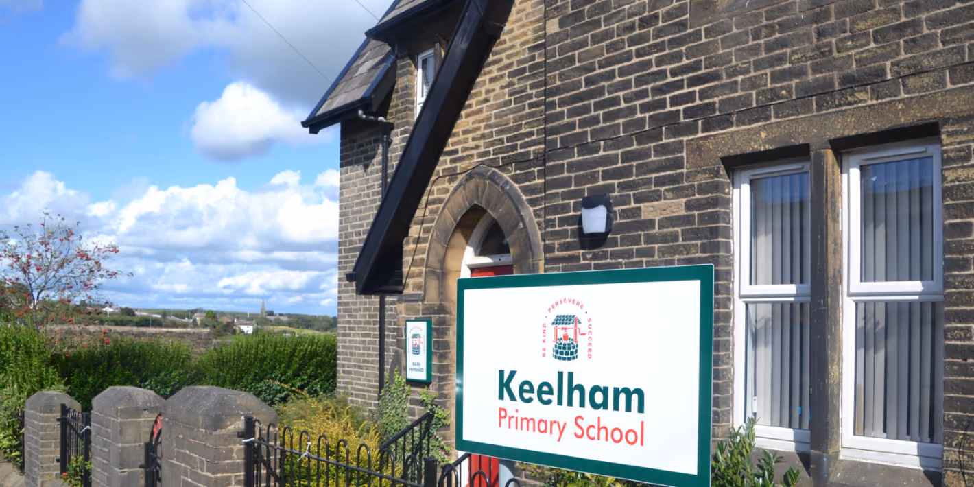 Brick building with a sign reading 'Keelham Primary School' under a partly cloudy blue sky.