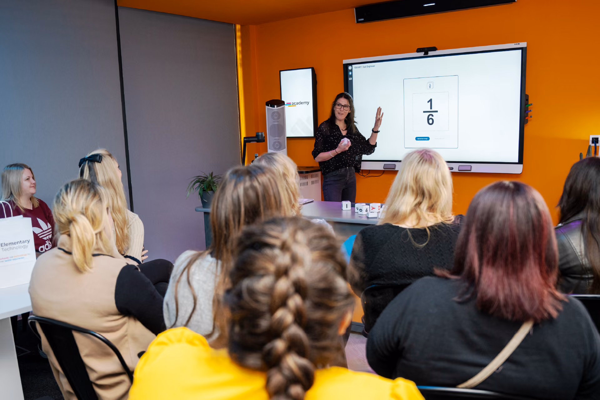 A woman instructs a group of teachers on how to use a SMART interactive touchscreen.