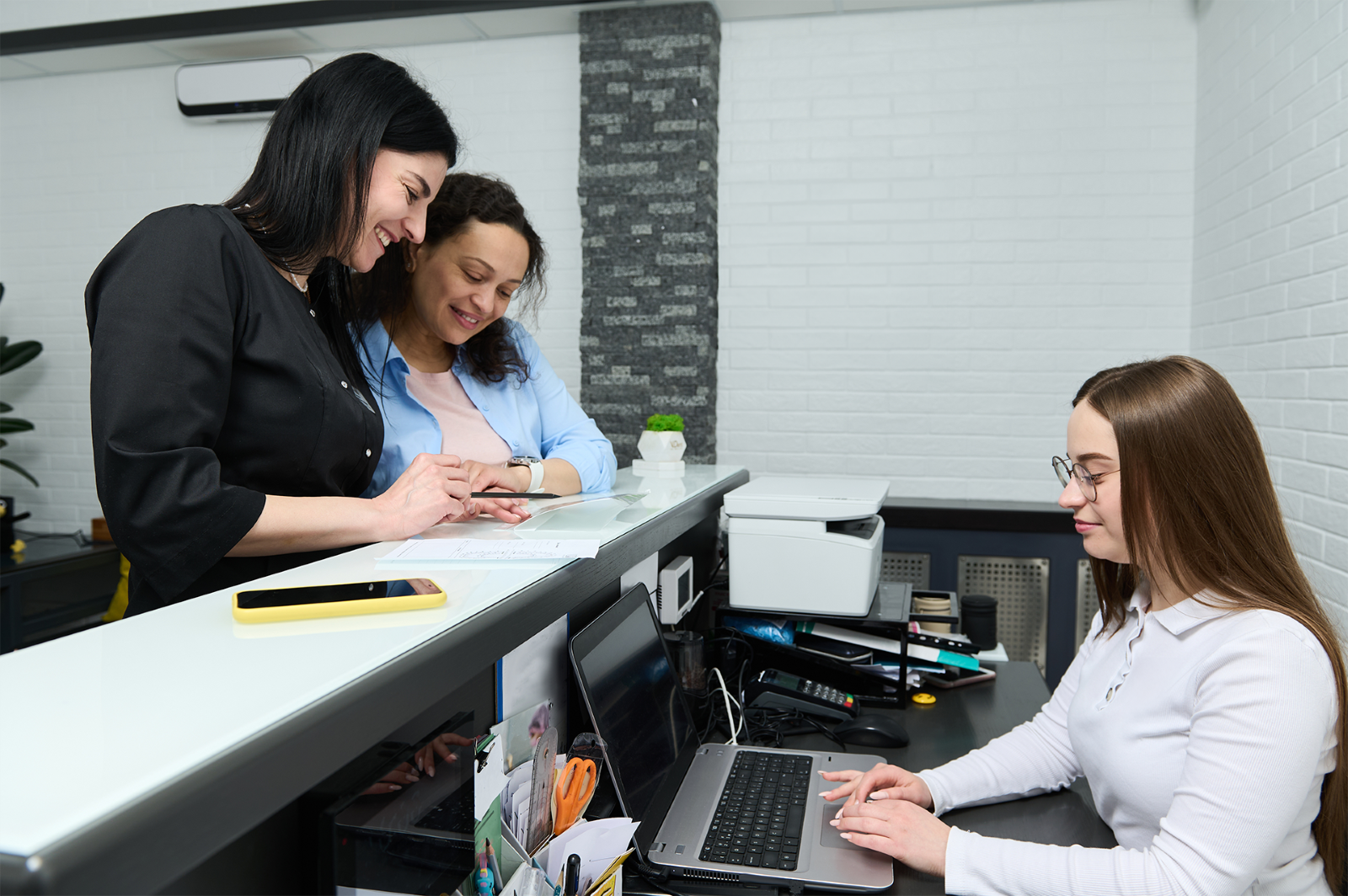 Two women checking into a busy clinic with a receptionist. h